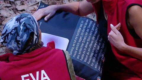 Die Kissenbombe platzt: Eva bekommt von Samira den Text auf ihrem bedruckten Kissen vorgelesen. Die Kissenbombe platzt: Eva bekommt von Samira den Text auf ihrem bedruckten Kissen vorgelesen.