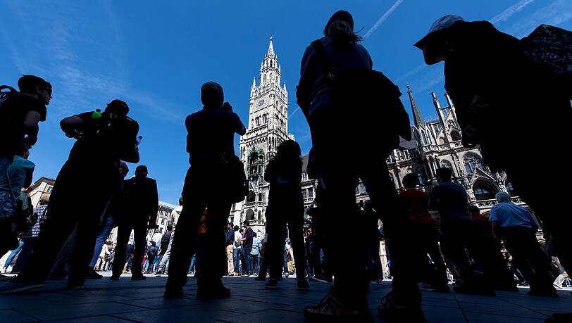 Touristen und Einheimische verfolgen das Glockenspiel auf dem Marienplatz in München. Touristen und Einheimische verfolgen das Glockenspiel auf dem Marienplatz in München.