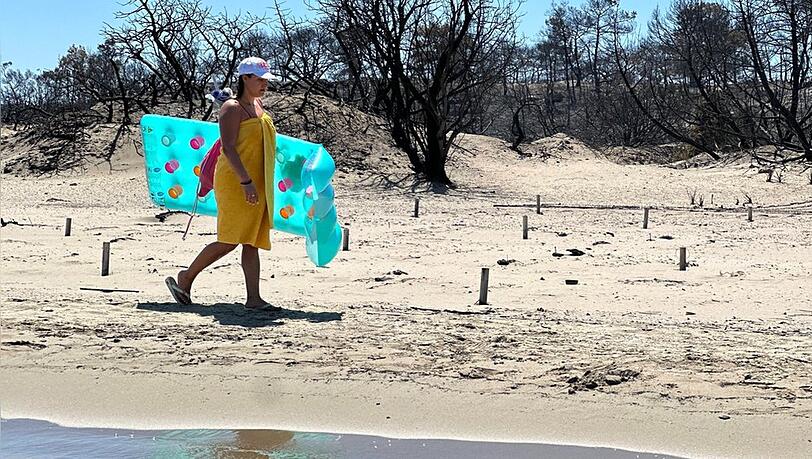Eine Touristin am Strand von Rhodos vor verbrannter Natur. Eine Touristin am Strand von Rhodos vor verbrannter Natur.