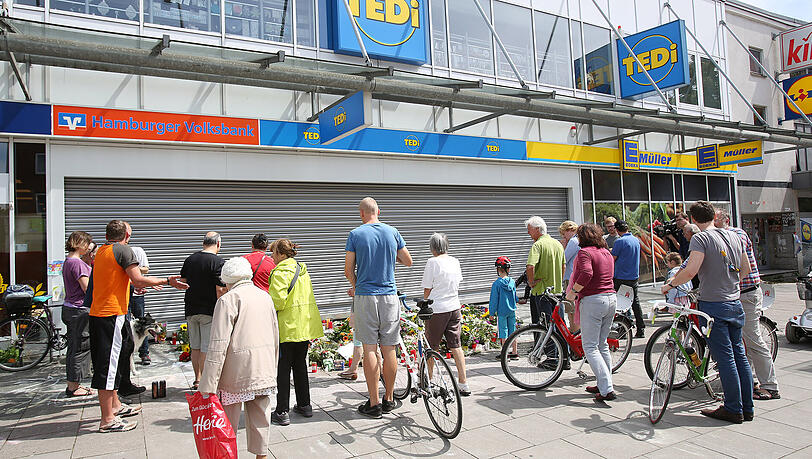 Passanten stehen vor dem Supermarkt in Hamburg-Barmbek, in dem ein Mann einen Menschen mit einem Messer getötet und sechs weitere verletzt hat. Passanten stehen vor dem Supermarkt in Hamburg-Barmbek, in dem ein Mann einen Menschen mit einem Messer getötet und sechs weitere verletzt hat.