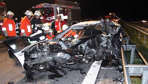 Einsatzkräfte stehen vor einem völlig zerstörten Auto. Einsatzkräfte stehen vor einem völlig zerstörten Auto.