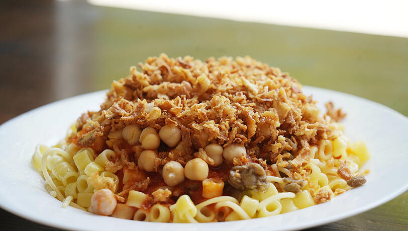 Koshari besteht aus Nudeln, Linsen, Kichererbsen, Tomatensoße und knusprigen Zwiebeln. Koshari besteht aus Nudeln, Linsen, Kichererbsen, Tomatensoße und knusprigen Zwiebeln.
