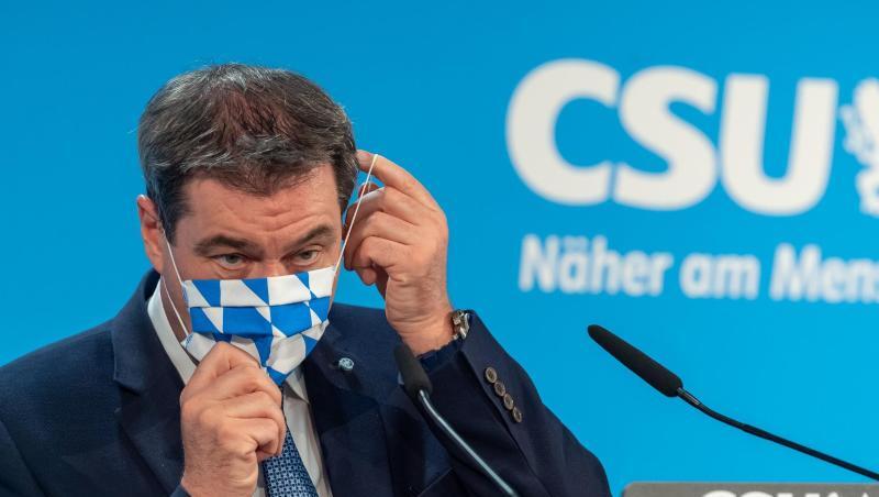 Markus Söder (CSU) steht auf einem Podium und setzt sich seine Mundschutzmaske auf. Foto: Peter Kneffel/dpa