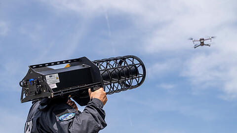 Ein Polizist steht während einer Demonstration im Rahmen der Eröffnung des Drohnenkompetenz- und -abwehrzentrum mit einem "Counter LAV Jammer HP 47 + PR V7" hinter einer Drohne. Damit lässt sich eine Drohne vom Himmel holen. Das 2025 beschlossene Drohnenkompetenz- und -abwehrzentrums (DKAZ) ist eine direkte Reaktion auf die steigende Zahl an Vorfällen mit Drohnen in Bayern, etwa über Flughäfen. Ein Polizist steht während einer Demonstration im Rahmen der Eröffnung des Drohnenkompetenz- und -abwehrzentrum mit einem "Counter LAV Jammer HP 47 + PR V7" hinter einer Drohne. Damit lässt sich eine Drohne vom Himmel holen. Das 2025 beschlossene Drohnenkompetenz- und -abwehrzentrums (DKAZ) ist eine direkte Reaktion auf die steigende Zahl an Vorfällen mit Drohnen in Bayern, etwa über Flughäfen.