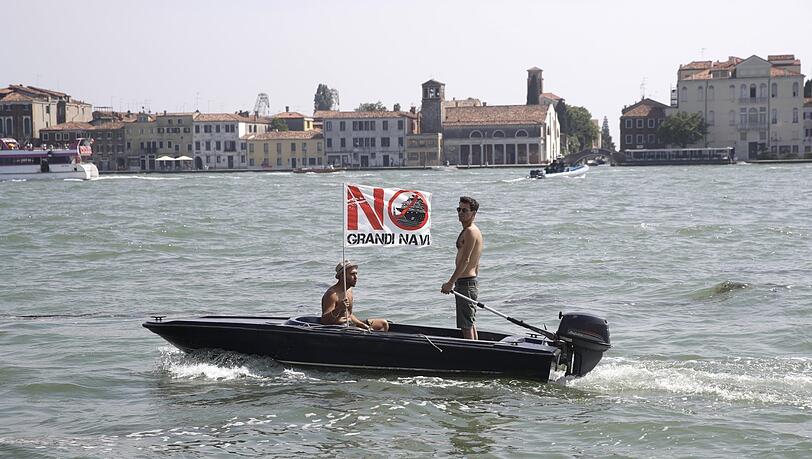Ein Mann auf einem kleinen Motorboot hält eine Fahne, auf der "Keine großen Schiffe" steht, im Rahmen einer Demonstration gegen Kreuzfahrtschiffe in der Lagune von Venedig. Ein Mann auf einem kleinen Motorboot hält eine Fahne, auf der "Keine großen Schiffe" steht, im Rahmen einer Demonstration gegen Kreuzfahrtschiffe in der Lagune von Venedig.