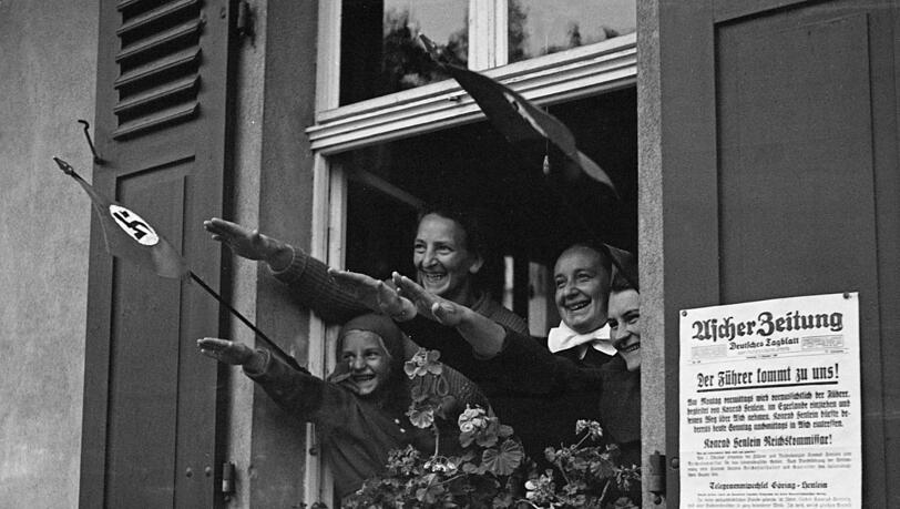 Mit Hakenkreuz-Fahnen und ausgestreckten Armen bejubelt diese Familie einen Besuch Adolf Hitlers in ihrer Heimatstadt. Ob die Frauen später mit ihren Familien über ihre Begeisterung gesprochen haben? Vermutlich haben sie eher geschwiegen. Mit Hakenkreuz-Fahnen und ausgestreckten Armen bejubelt diese Familie einen Besuch Adolf Hitlers in ihrer Heimatstadt. Ob die Frauen später mit ihren Familien über ihre Begeisterung gesprochen haben? Vermutlich haben sie eher geschwiegen.